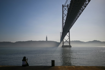 Une femme assise sur les bords du Tage près du pont du 25 avril dans le quartier touristique de Belem, à Lisbonne, le 19 novembre 2024 - PATRICIA DE MELO MOREIRA (AFP)