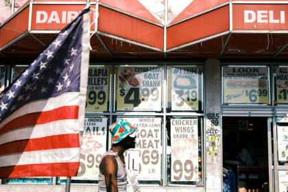 Une personne passe devant une épicerie et un drapeau américain dans le quartier de Flatbush, surnommé "Little Haiti", dans l'arrondissement de Brooklyn à New York, aux Etats-Unis, le 15 juillet 2025 - CHARLY TRIBALLEAU (AFP)
