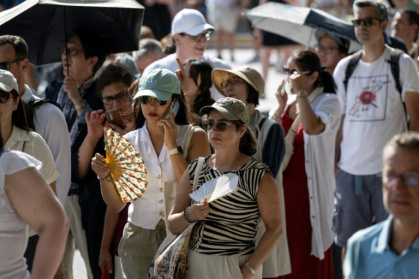 Des touristes avec des éventails devant la cathédrale Notre-Dame, le 16 août 2025 à Paris - Martin LELIEVRE (AFP)