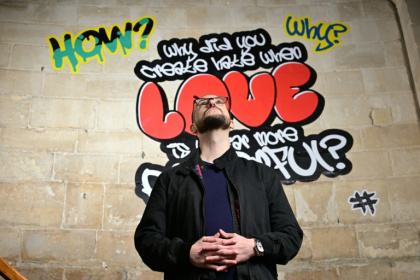 Le poète Alex Vellis, devant des graffitis de l'exposition "Hear us" ("Entends-nous"), sur les murs de la cathédrale de Canterbury (sud de l'Angleterre) le 16 octobre 2025 - Ben STANSALL (AFP)