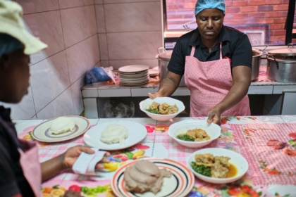 Des cuisiniers s'apprêtent à servir un plat contenant du sadza, une bouillie épaisse, au restaurant de Sis Phatis qui vend de la nourriture traditionnelle, à Bulawayo (Zimbabwe), le 15 mai 2026 - Zinyange AUNTONY (AFP)