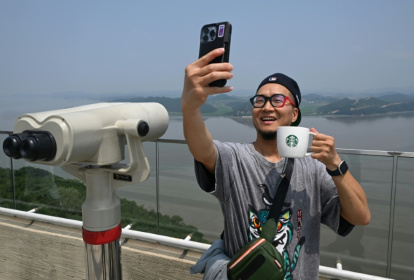 Un touriste prend un selfie avec une tasse Starbucks devant la Corée du Nord depuis une plate-forme d'observation sud-coréenne située à l'Écoparc de la Paix d'Aegibong, à Gimpo, le 1er juillet 2026 - Jung Yeon-je (AFP)