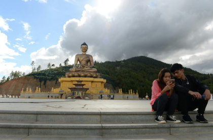 Un couple assis regarde l'écran d'un téléphone portable à côté d'une statue de Bouddha à Thimphou, la capitale du Bouthan, le  25 août 2018 - ARUN SANKAR (AFP)